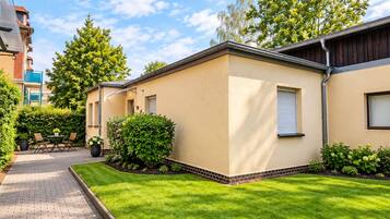 A residential building with a paved driveway, a lawn, and a small patio area with outdoor furniture.
