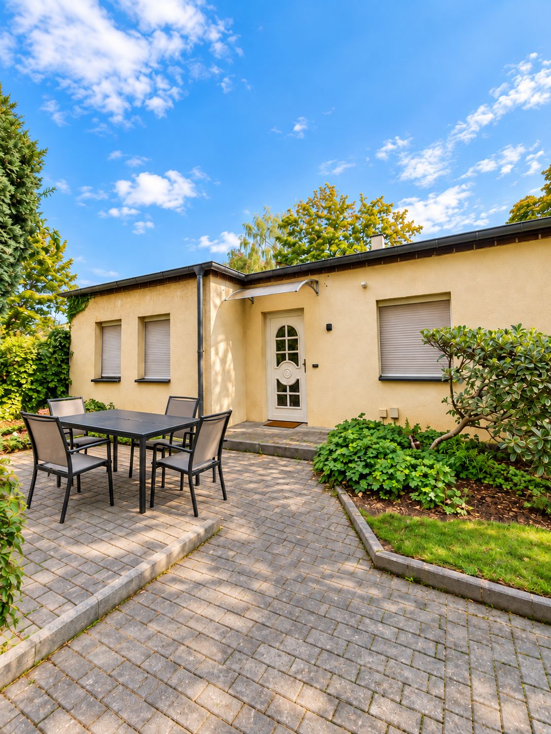Eine Terrasse mit Tisch und Stühlen, einer Tür und einem kleinen Garten.