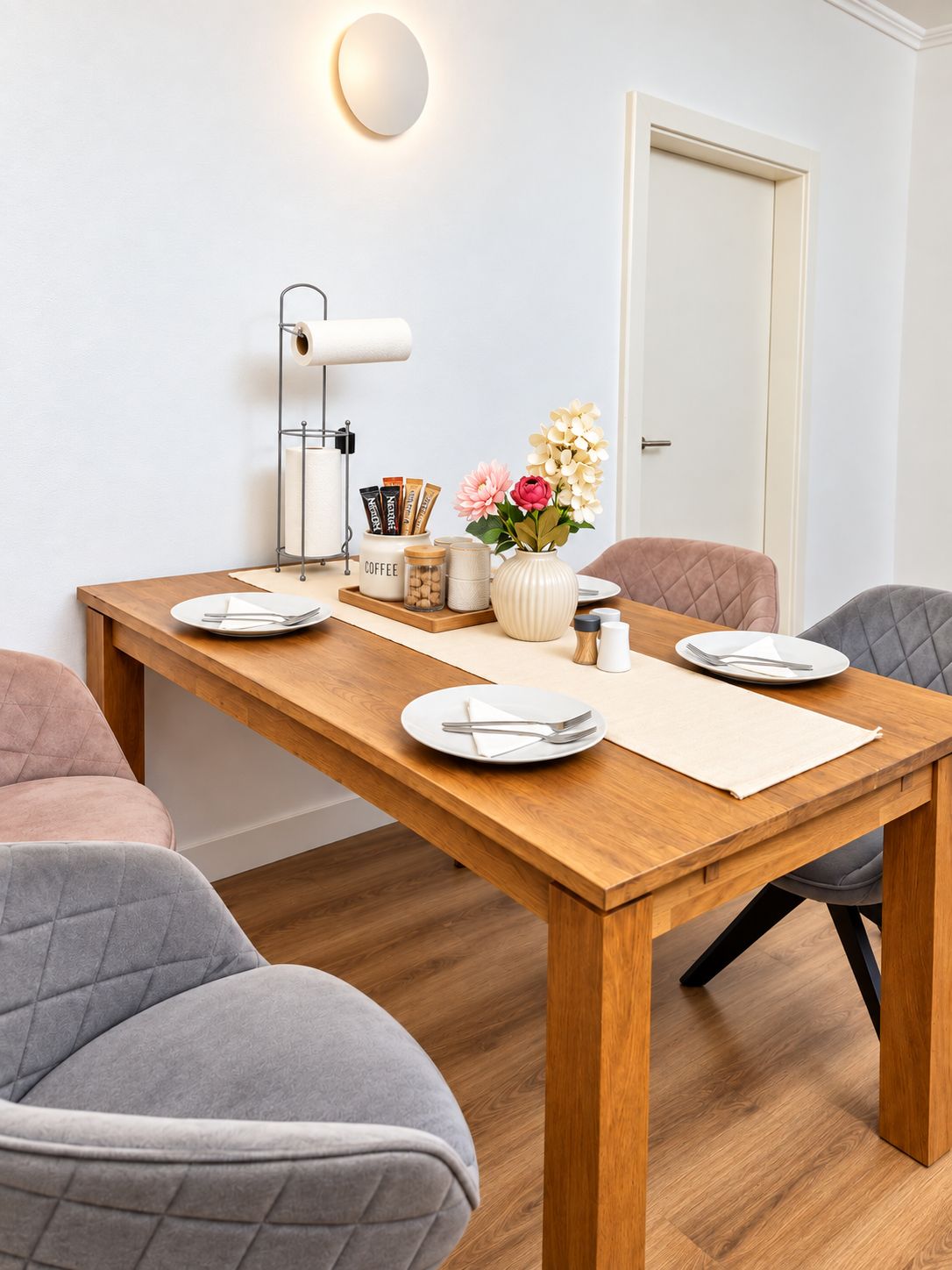 A dining area with a wooden table, chairs, a wall-mounted lamp, and a door.