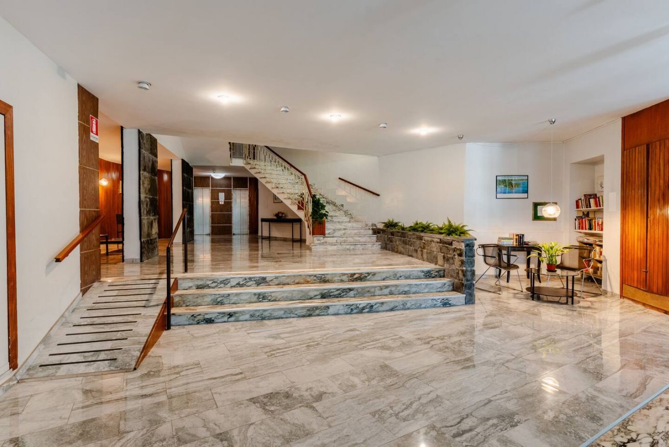 Eine Hotelhalle mit einer Marmortreppe, einem Empfangsbereich und einer Sitzecke mit Pflanzen.