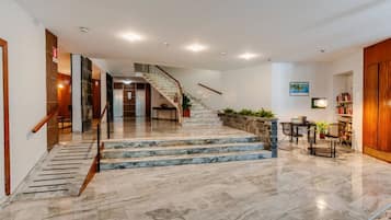 Eine Hotelhalle mit einer Marmortreppe, einem Empfangsbereich und einer Sitzecke mit Pflanzen.