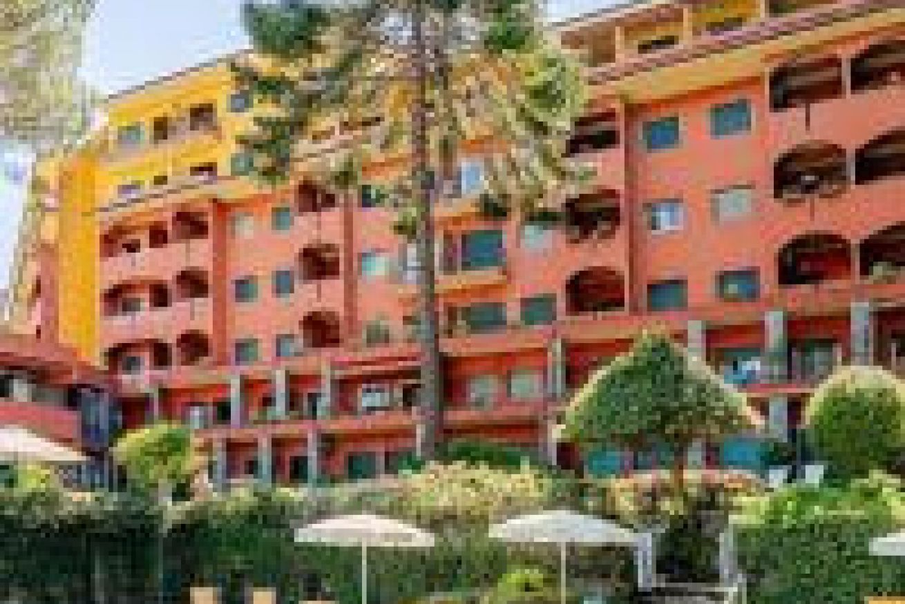 Een meerlaags hotel met balkons, een centrale binnenplaats met bomen en buiten zitplaatsen.