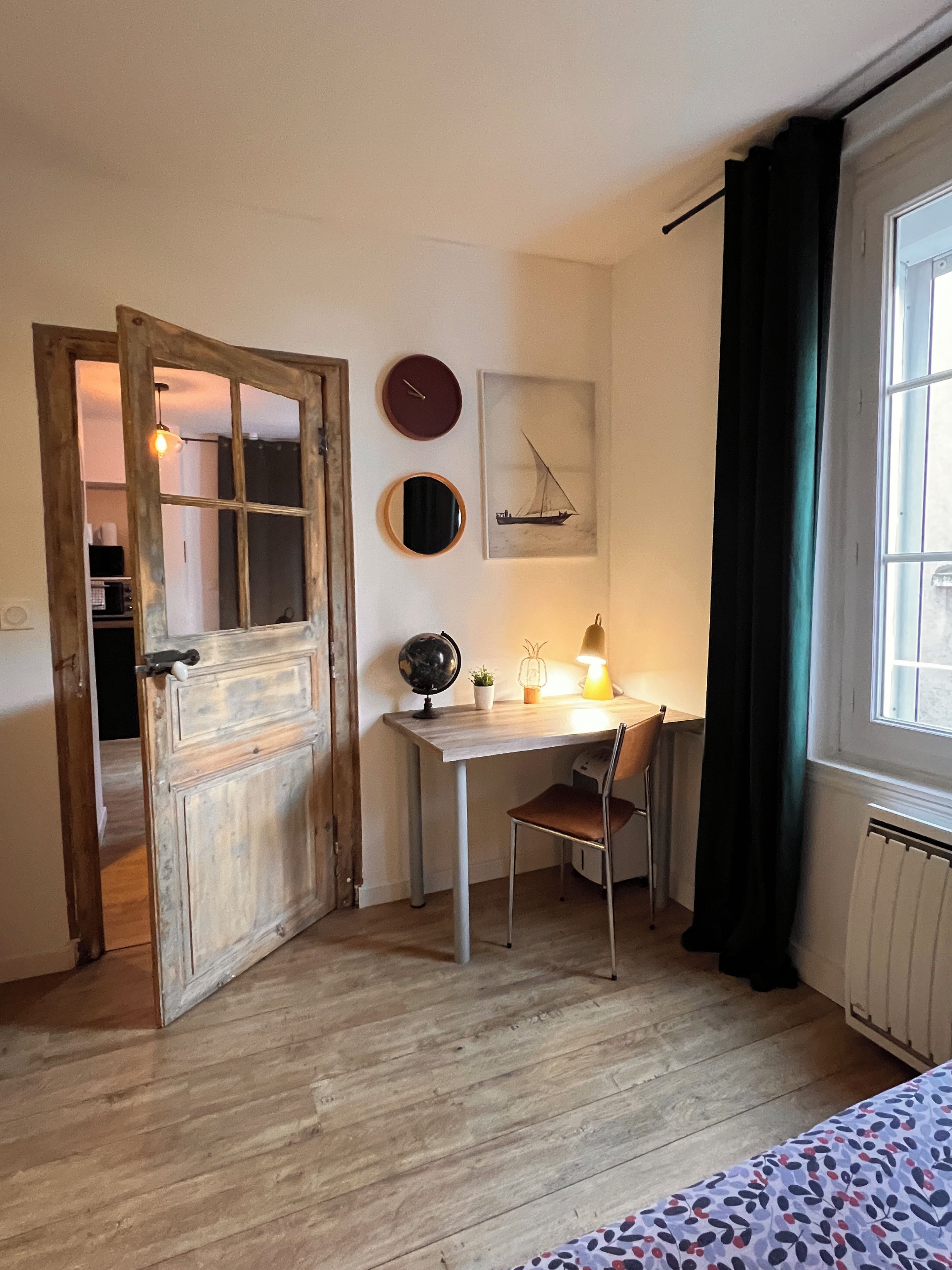 Een kamer met een houten deur, een bureau met stoel, een wereldbol, een lamp en een raam met gordijnen.