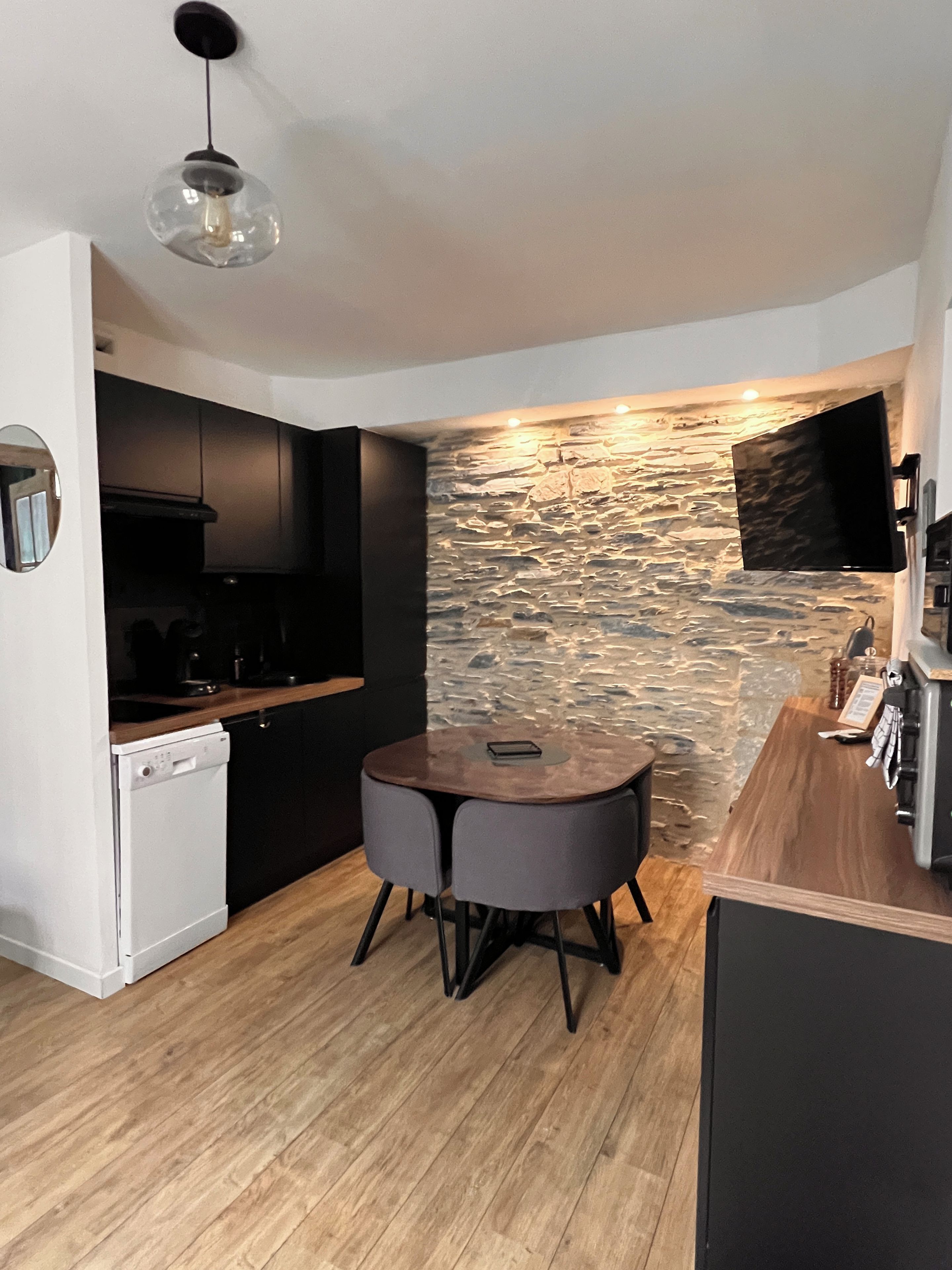 A modern kitchen with a stone wall, a round dining table, and a built-in dishwasher.