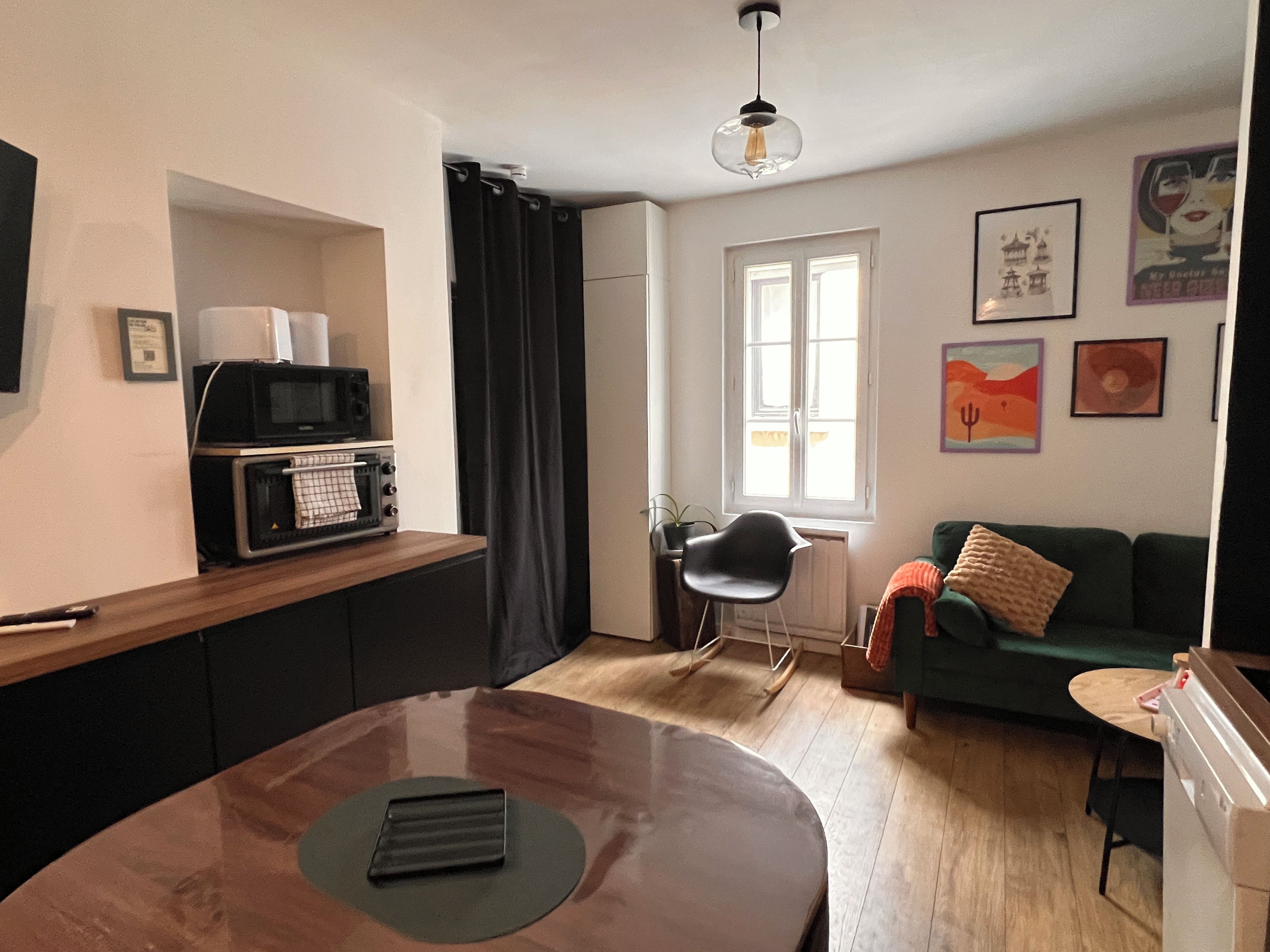 A compact living space with a kitchenette, a dining table, a sofa, and a window providing natural light.