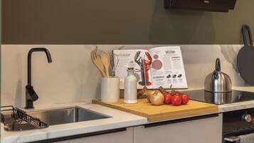 A kitchen with a modern faucet, a wooden cutting board with vegetables, a kettle, and a cookbook.