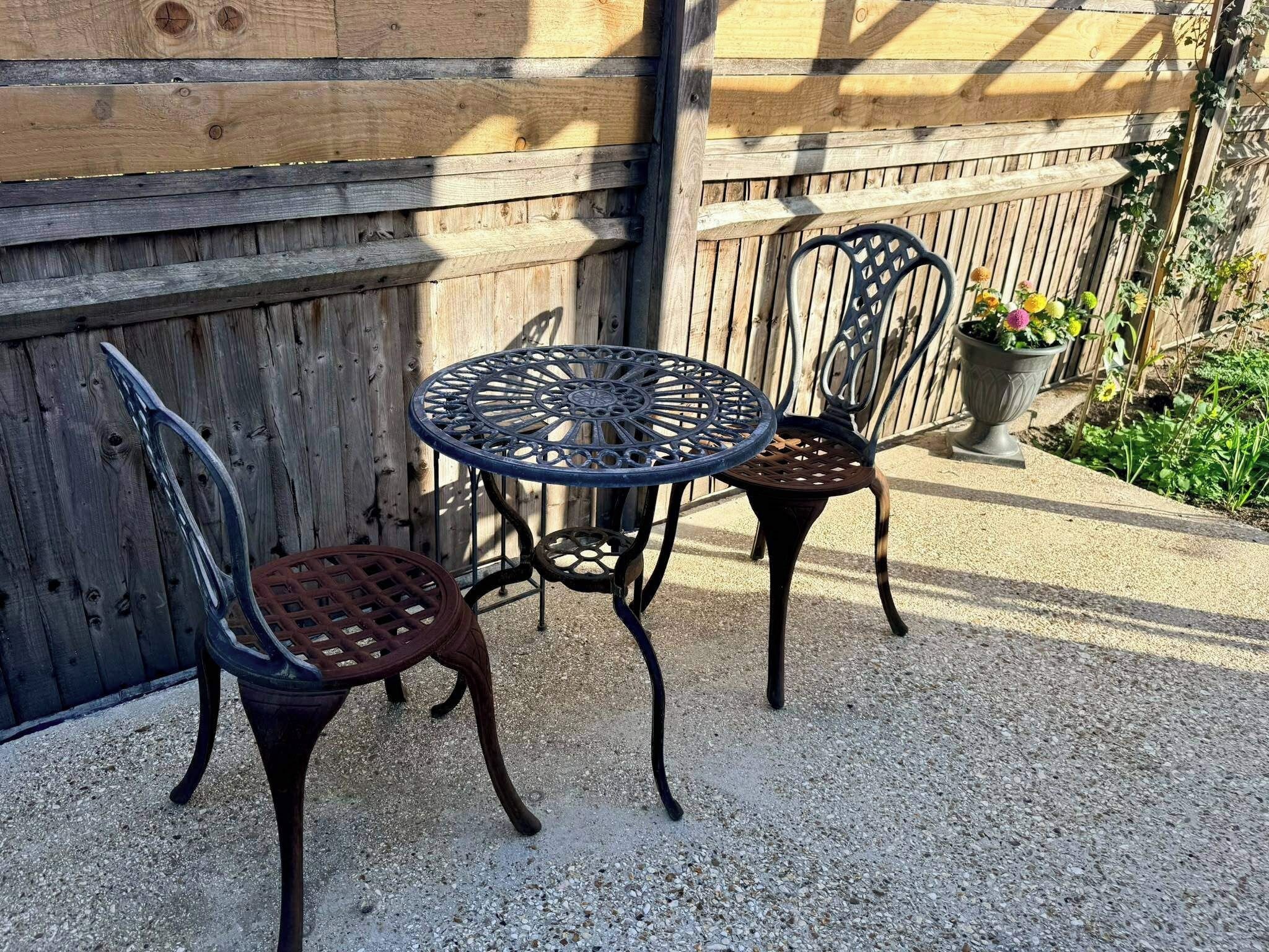 A patio area with a round table and two chairs, a wooden fence, and a potted plant.