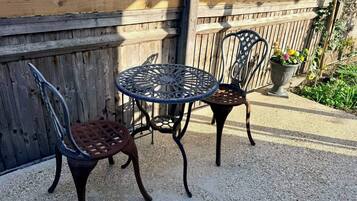 A patio area with a round table and two chairs, a wooden fence, and a potted plant.