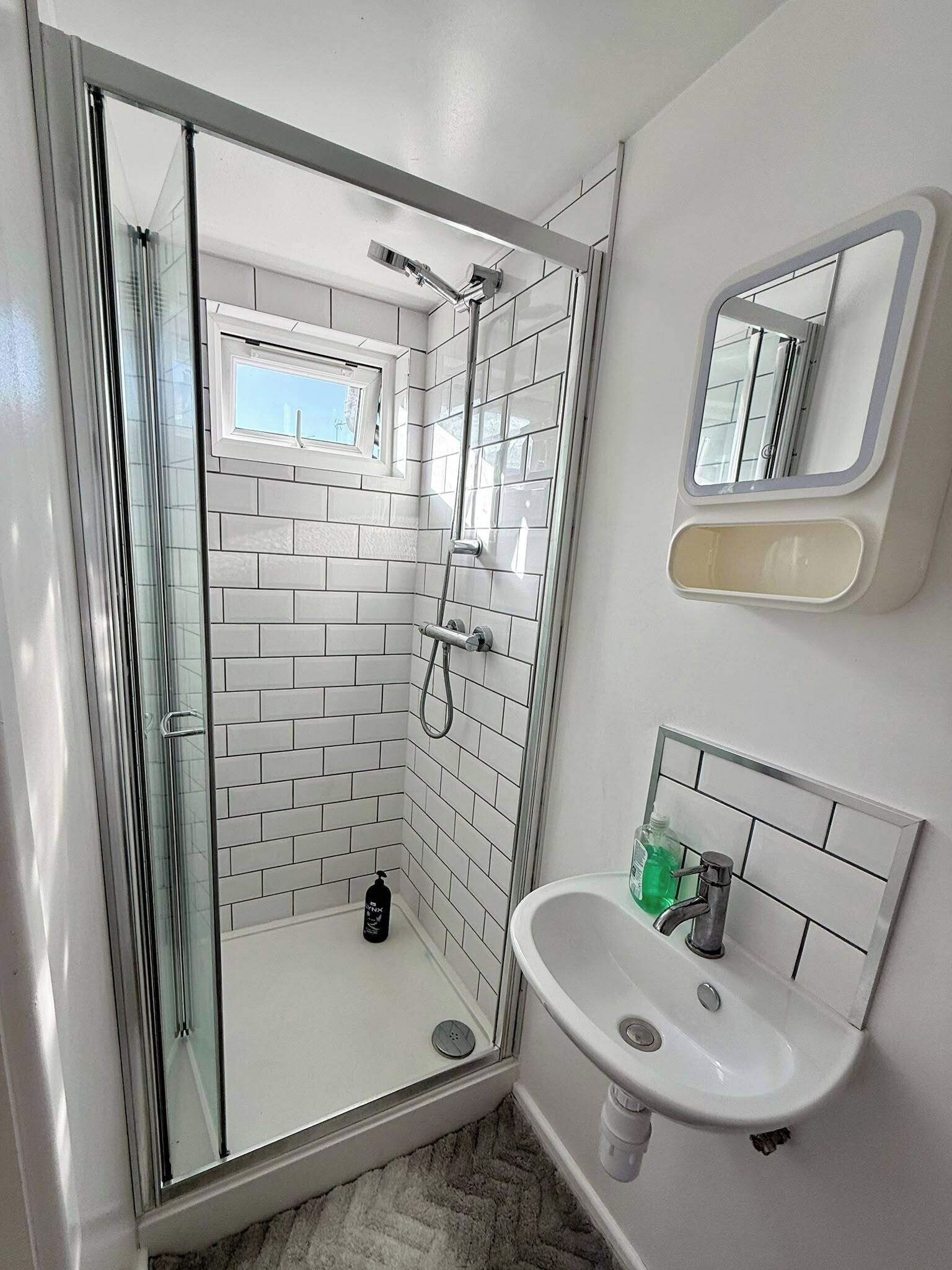 A modern bathroom with a glass-enclosed shower, a white sink, and a mirror.
