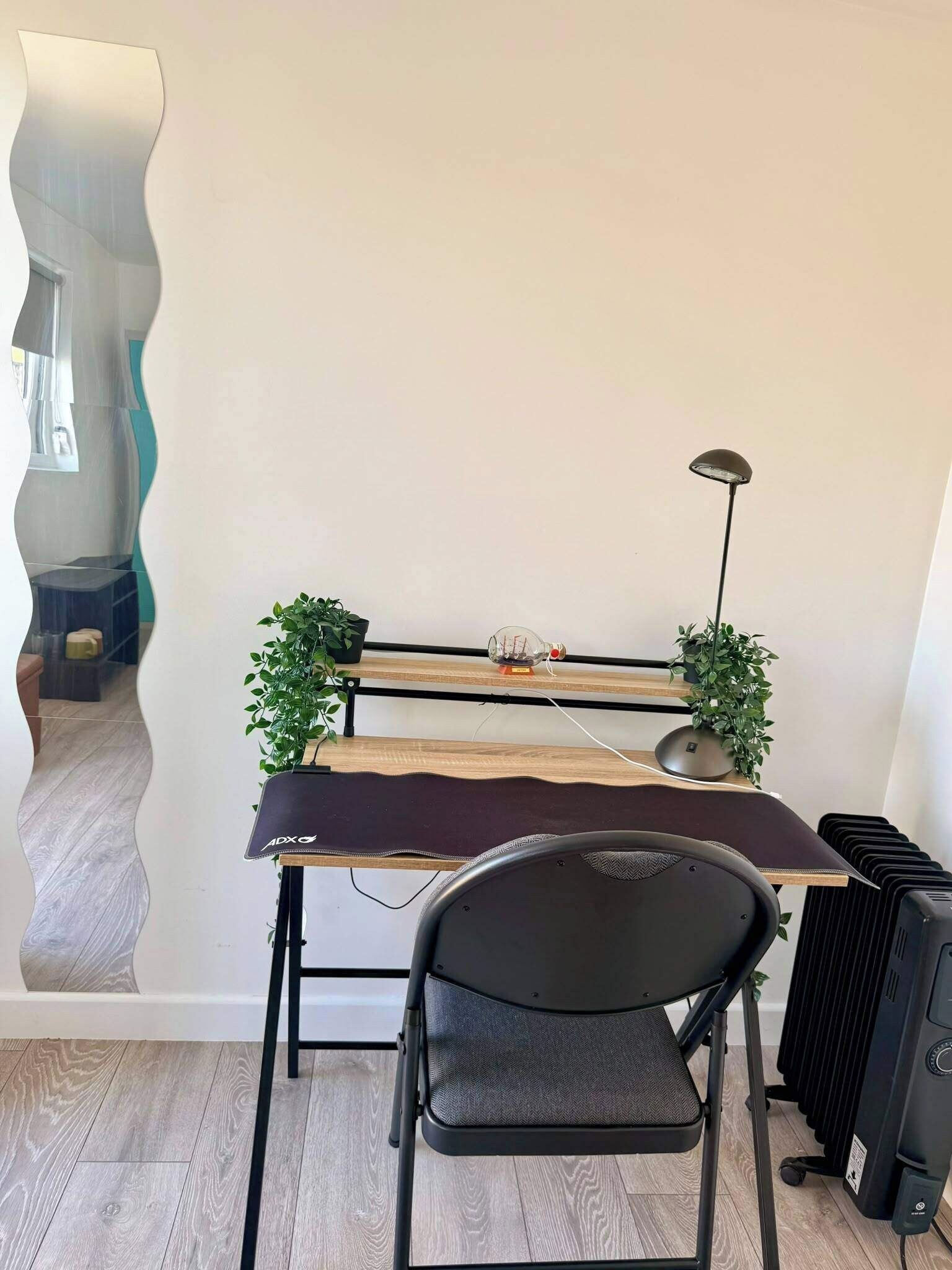 A compact workspace with a foldable desk, a chair, a lamp, and a radiator.