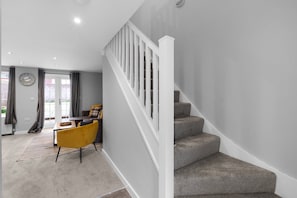 Un interior moderno con una escalera, una zona de comedor con una silla amarilla y un suelo cubierto de moqueta gris.