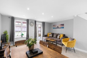 A modern living room with a sofa, coffee table, and dining area. - Dudley Gardens 3 Bedroom 1 Bath Hse (Poole)