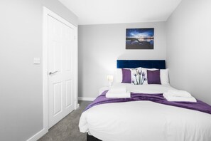 Une chambre d’hôtel avec un lit, une table de chevet, un tableau et une porte.