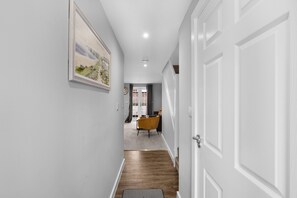 A hallway with a wooden floor, a door on the right, and a painting on the left wall. - Dudley Gardens 3 Bedroom 1 Bath Hse (Poole)