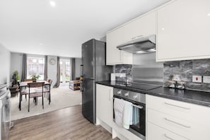 A modern kitchen with stainless steel appliances, a marble backsplash, and a dining area with a view. - Dudley Gardens 3 Bedroom 1 Bath Hse (Poole)