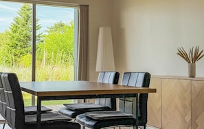 Een eetruimte met een tafel, stoelen, een lamp en uitzicht op groen.