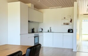 A modern kitchen with white cabinetry, a wooden dining table, and a black chair. - 2 bedroom beautiful home in Slagelse (Slagelse)
