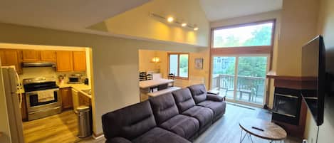 A modern living room with a sectional sofa, a fireplace, and a dining area with a kitchen in the background.