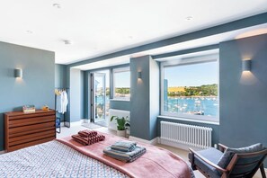 Une chambre à coucher comprenant un lit, une commode, une chaise, une fenêtre donnant sur un port de plaisance et un radiateur.