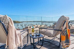 A balcony with a view of a harbor, a bottle of wine, and a glass on a small table. - Panoramic harbour views & fireplace | Porthva (Cornwall)