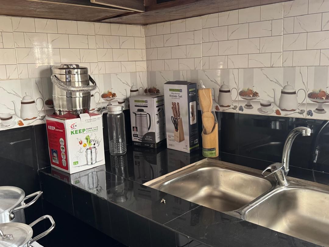 A kitchen with a stainless steel sink, a kettle, and various kitchen appliances and utensils.