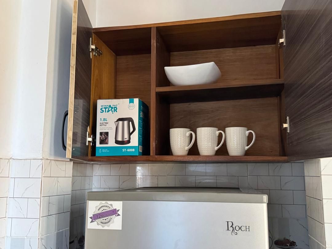 A kitchen with a built-in microwave, a Bosch refrigerator, and a shelf with a kettle and cups.