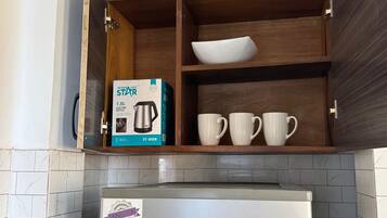 A kitchen with a built-in microwave, a Bosch refrigerator, and a shelf with a kettle and cups.