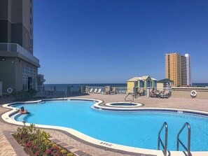 A swimming pool with a curved design, surrounded by lounge chairs and a building with a balcony. - Family Friendly Gulf View Free Beach Chairs (Mar. 2027) & Activities Daily! (Panama City Beach)