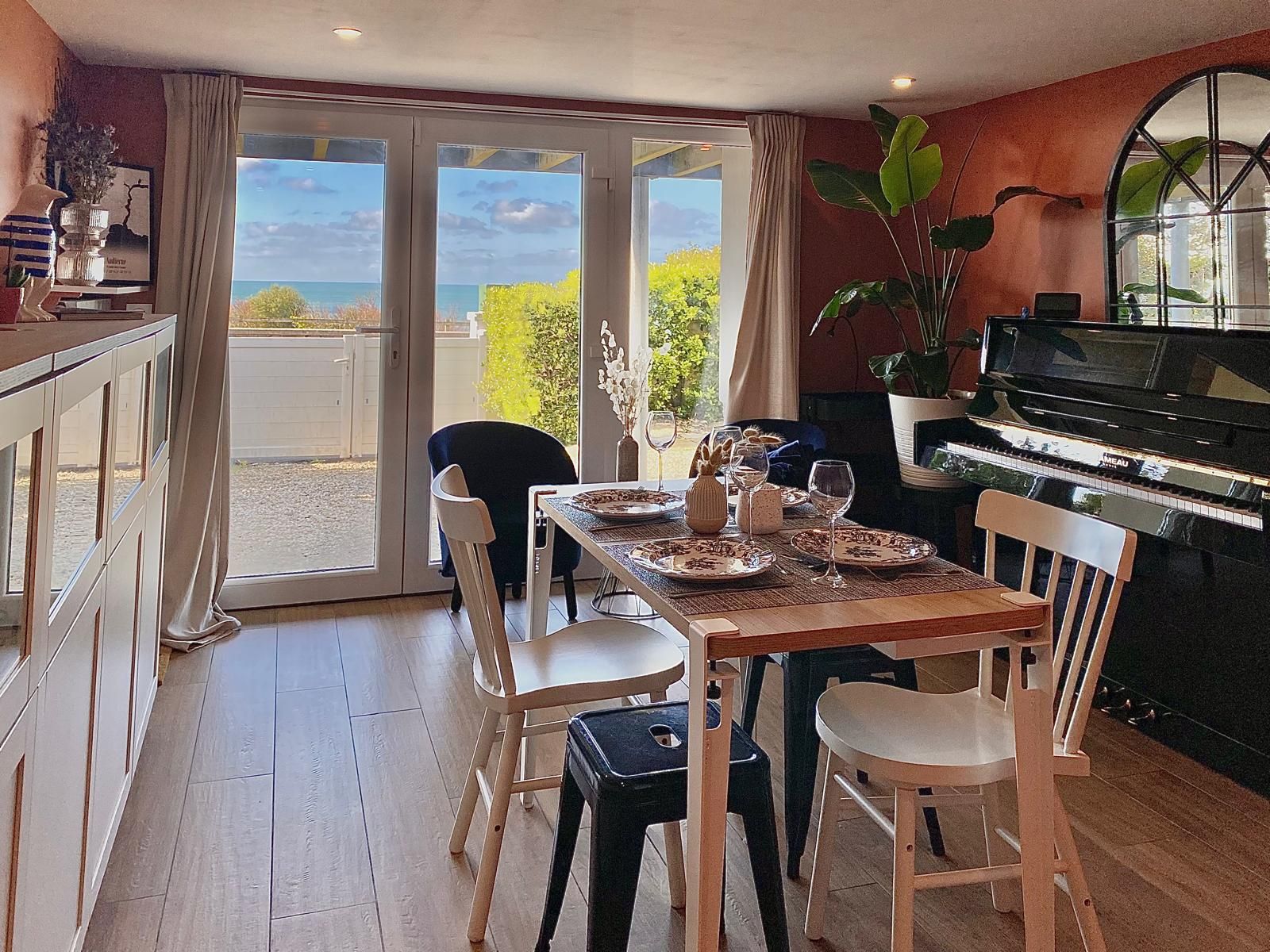 A dining area with a piano, a table set for four, and a view through a glass door.