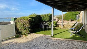 A covered outdoor area with a gravel patio, a grassy lawn, and two lounge chairs.