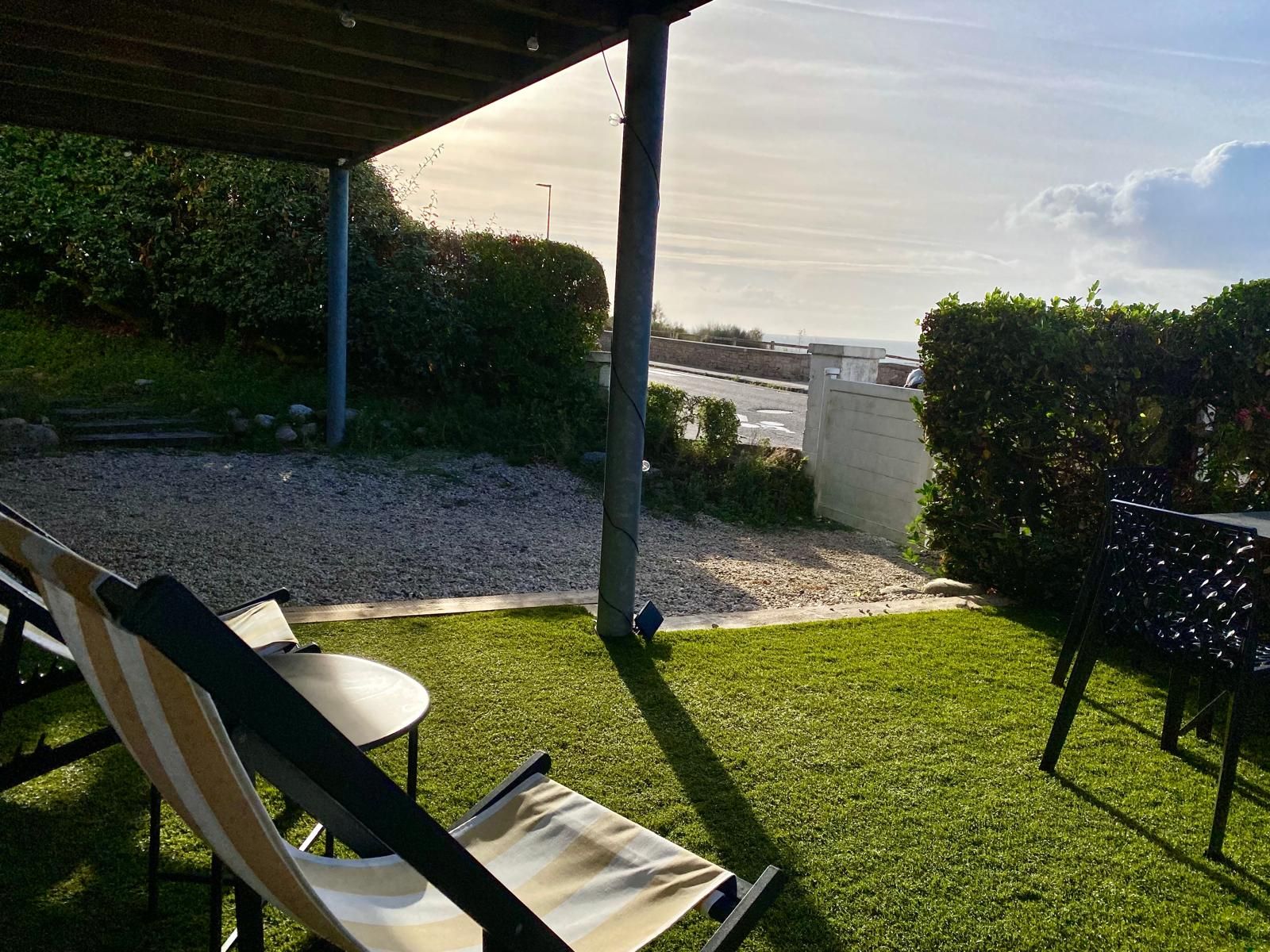 A patio area with a view of the sea, a lawn, and a seating area with a table and chairs.