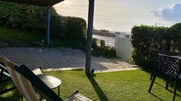 A patio area with a view of the sea, a lawn, and a seating area with a table and chairs.