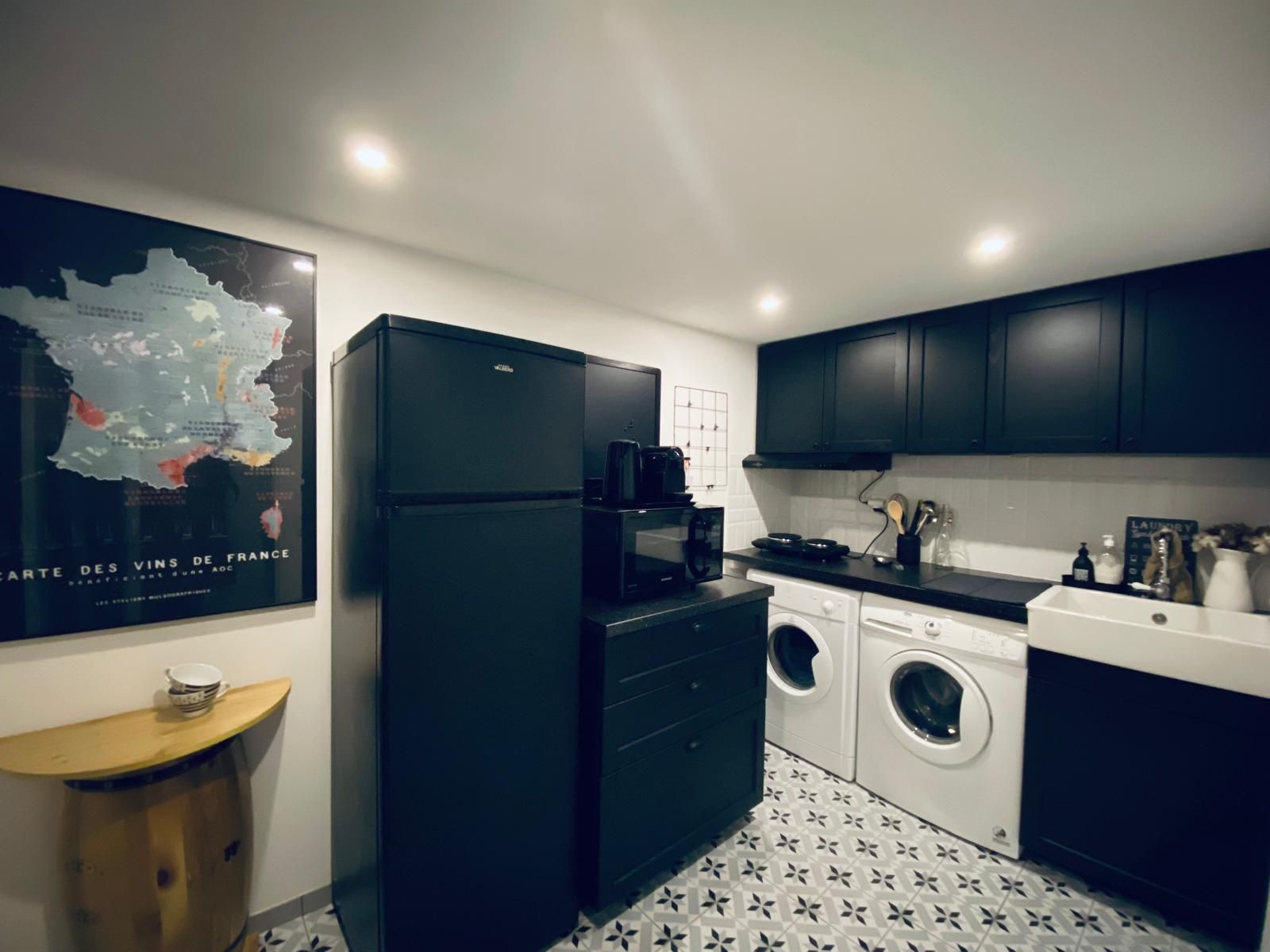 A compact kitchen with a refrigerator, microwave, washing machine, and a coffee maker.