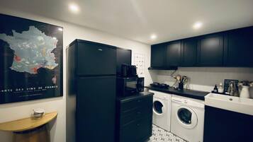 A compact kitchen with a refrigerator, microwave, washing machine, and a coffee maker.