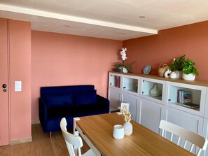 Habitació amb taula de dinar de fusta, cadires blanques, un sofà blau i un armari amb portes de vidre.