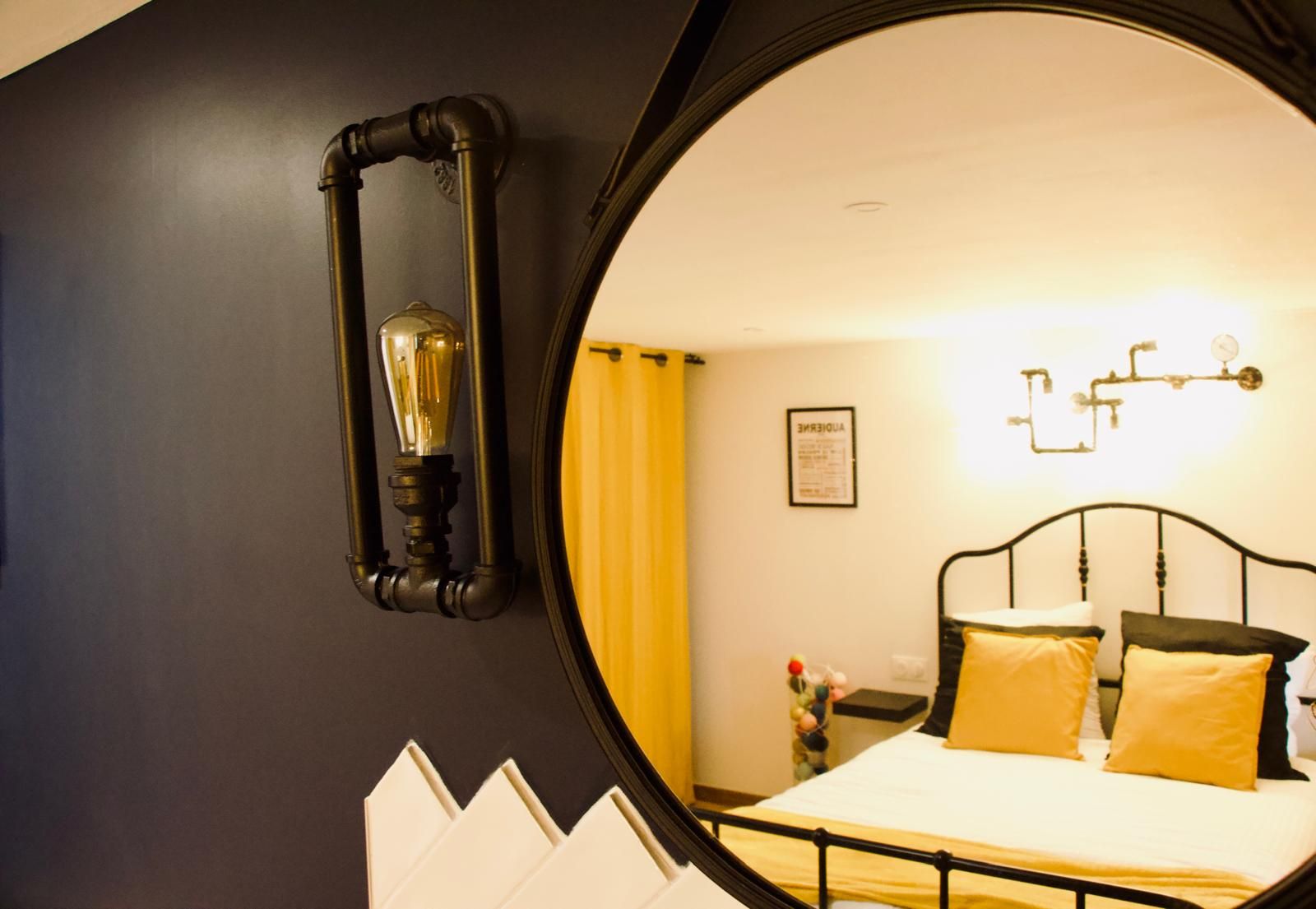 A bedroom with a bed, a mirror, and a wall-mounted light fixture.