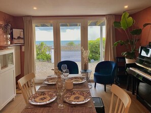 Una zona de menjador amb una taula ben posada per a quatre, un piano i vista al mar.