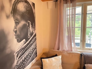 A room with a large portrait on the wall, a window with sheer curtains, and a sofa with patterned cushions. - 5 Person Holiday Home in Uddevalla (Uddevalla)