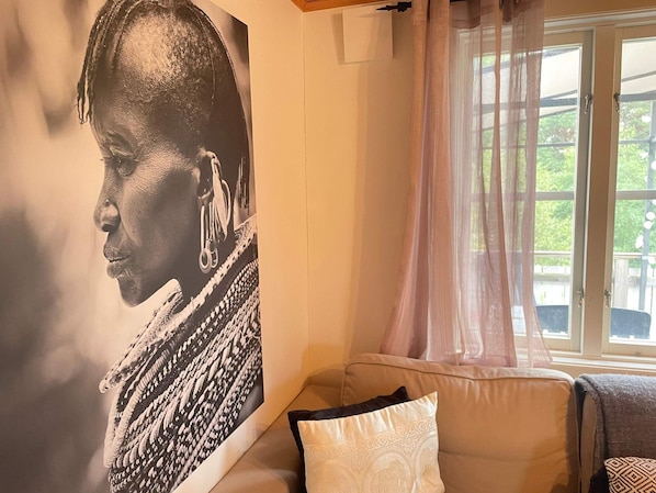 Una habitación con un retrato grande en la pared, una ventana con cortinas translúcidas y un sofá con cojines estampados.