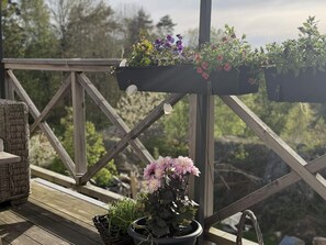 Una terraza de madera con una silla de mimbre y plantas en macetas.