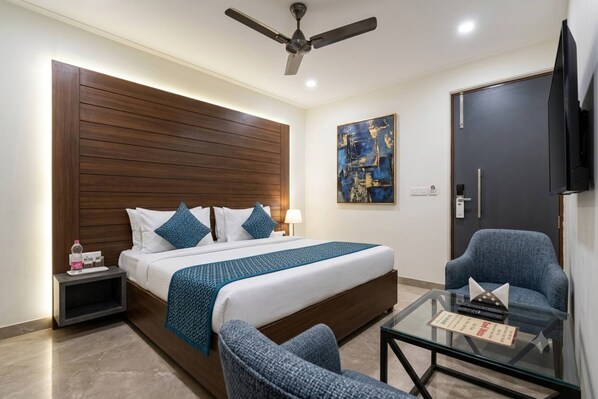 A hotel room with a bed, a desk, a chair, a TV, and a ceiling fan. - NewDelhi Hotel Citizen 1 (New Delhi)
