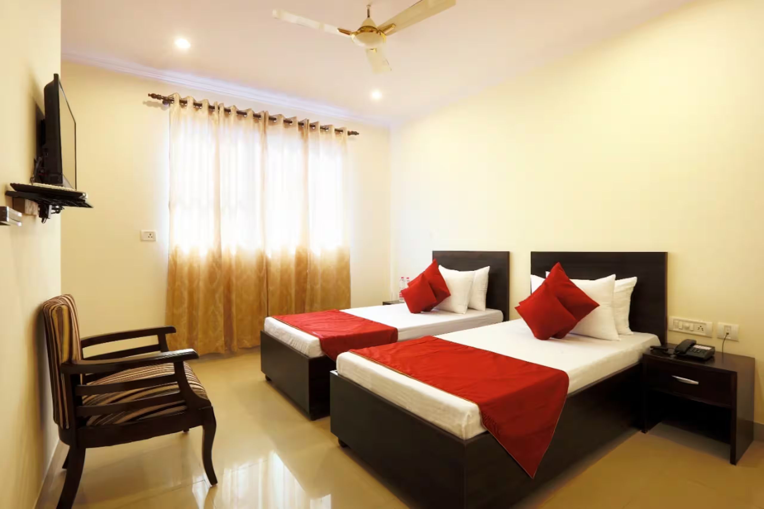 A hotel room with two beds, a chair, a nightstand, and a ceiling fan.