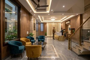Eine Hotellobby mit einer Rezeption, einer Sitzecke mit Stühlen, einem Deckenventilator und einer Treppe.
