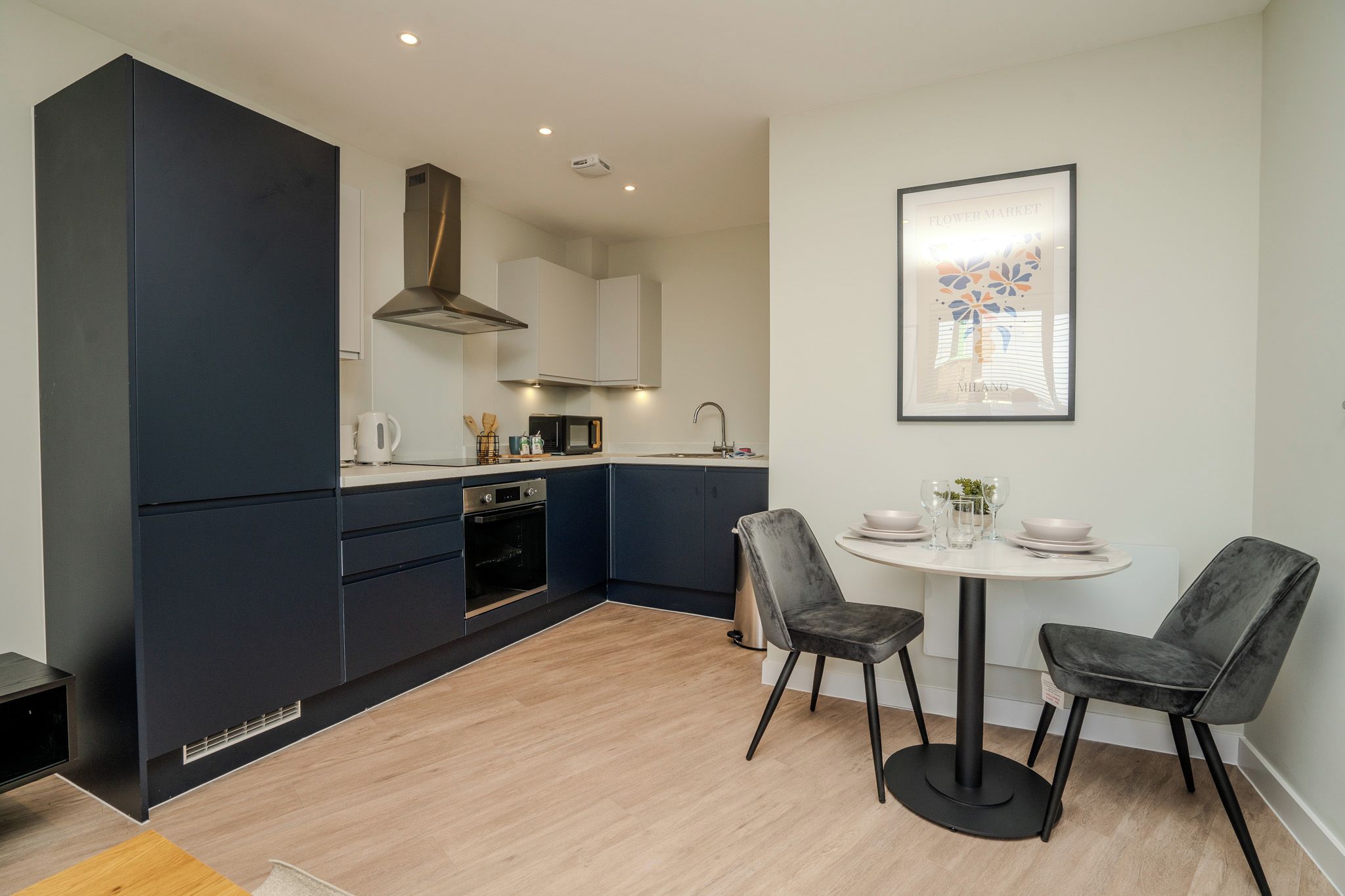 A modern kitchen with dark cabinetry, a built-in oven, and a dining area with two chairs and a small table.
