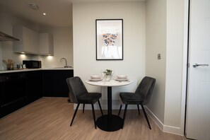 Una cocina moderna con comedor, que incluye una mesa blanca con dos sillas, un cuadro enmarcado sobre la mesa y una puerta blanca a la derecha.