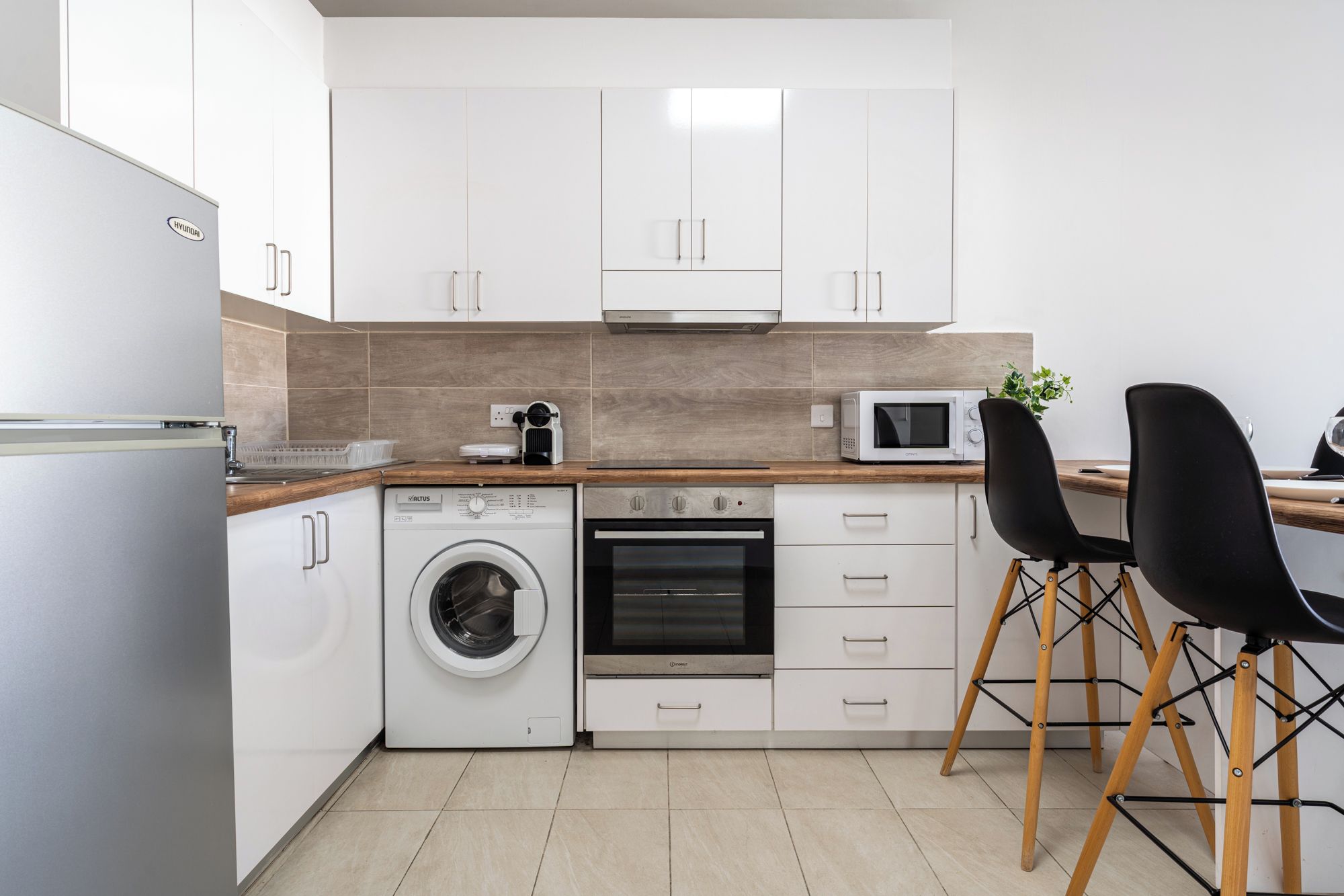 A modern kitchen with a washing machine, oven, microwave, and wooden countertop.