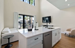 A modern kitchen with a built-in dishwasher, a coffee maker, and a flat-screen TV mounted on the wall. - Cassa Orlando: Luxury Poolside 2BR/2BA Unit 104 (Orlando)