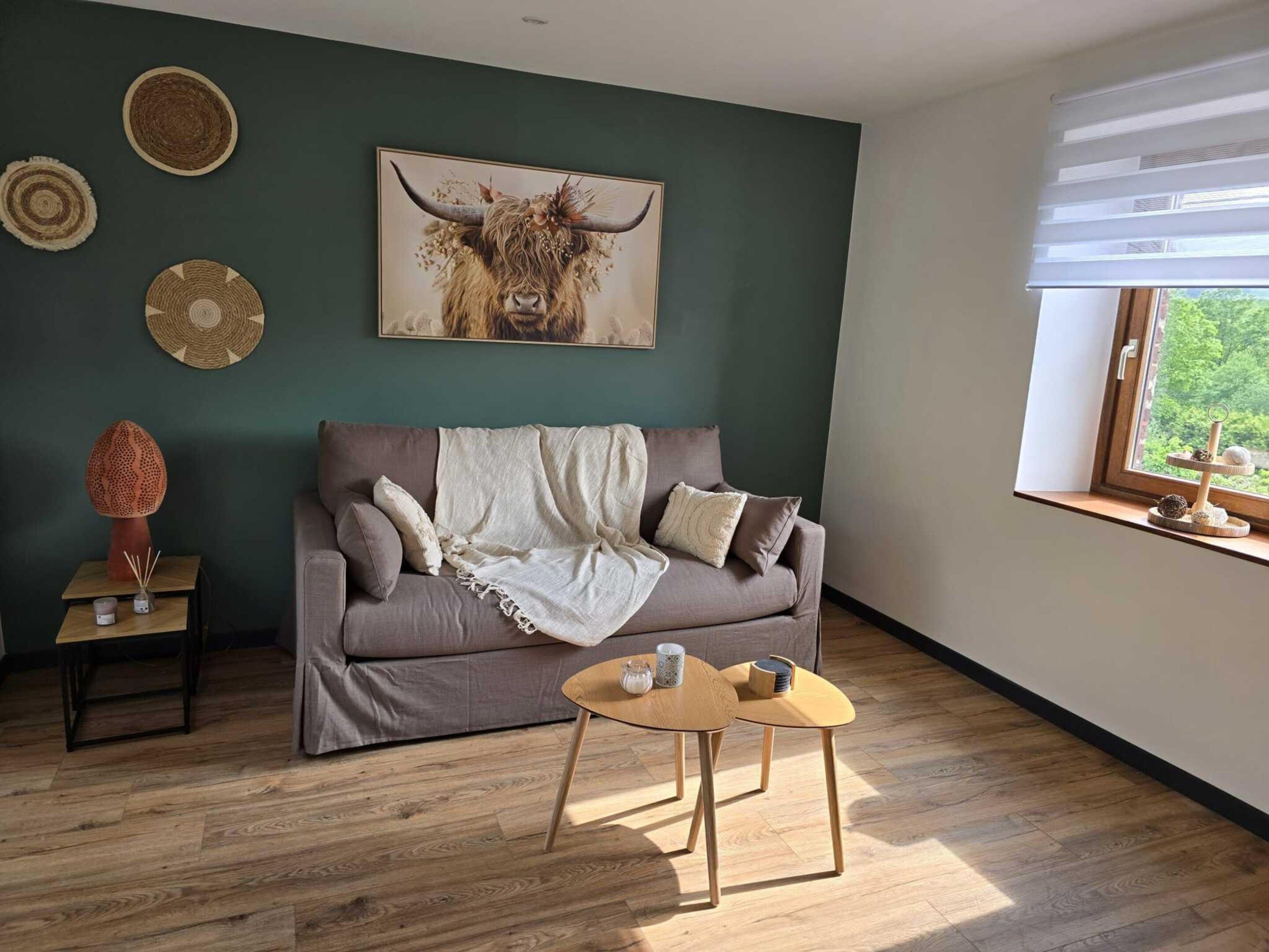 Una sala de estar con sofá, una mesita de centro, una obra de arte colgada en la pared de un toro, y una ventana con vistas.