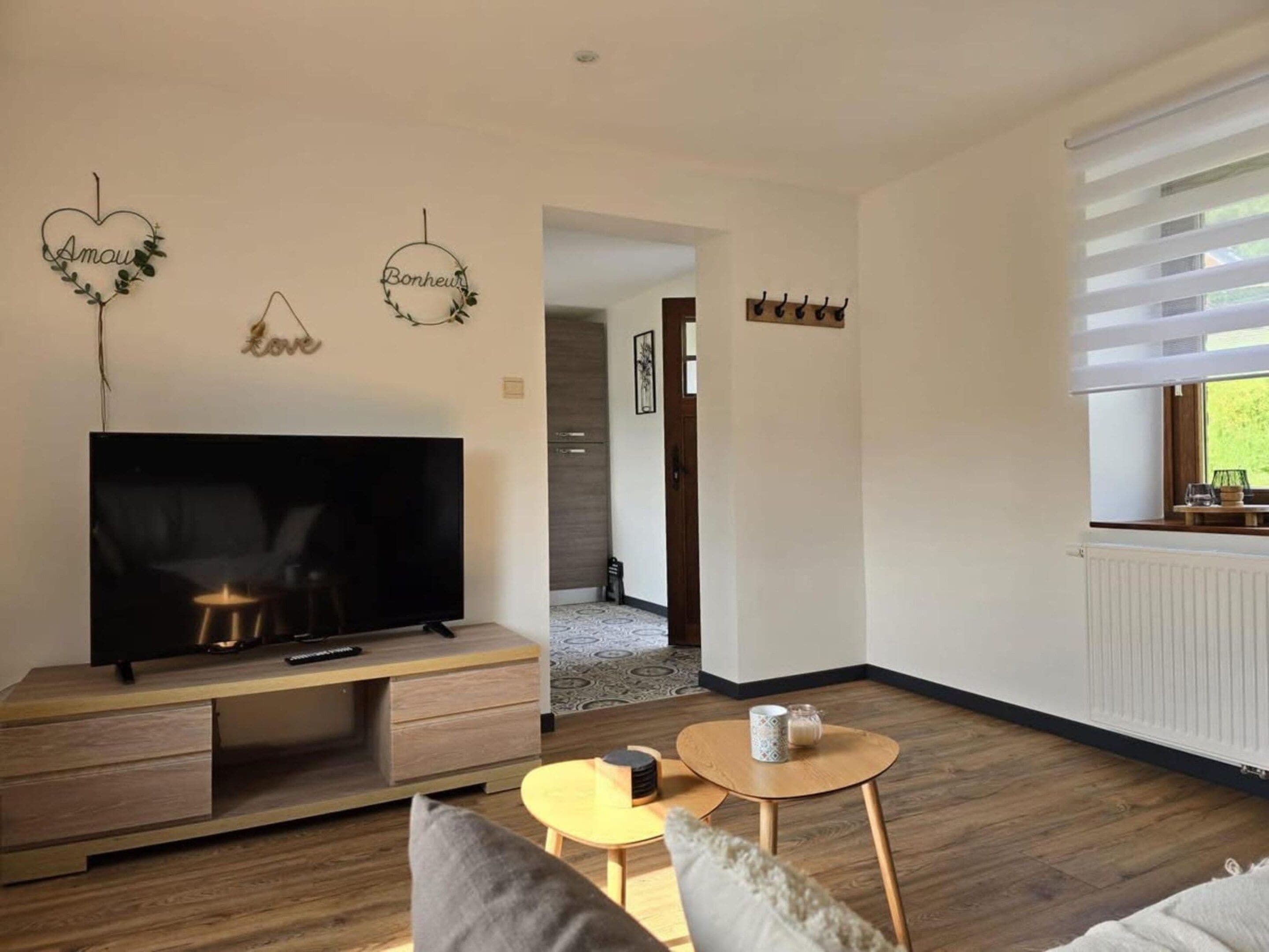 A modern living room with a flat-screen TV on a wooden TV stand, a small round table with a cup, and a sofa.