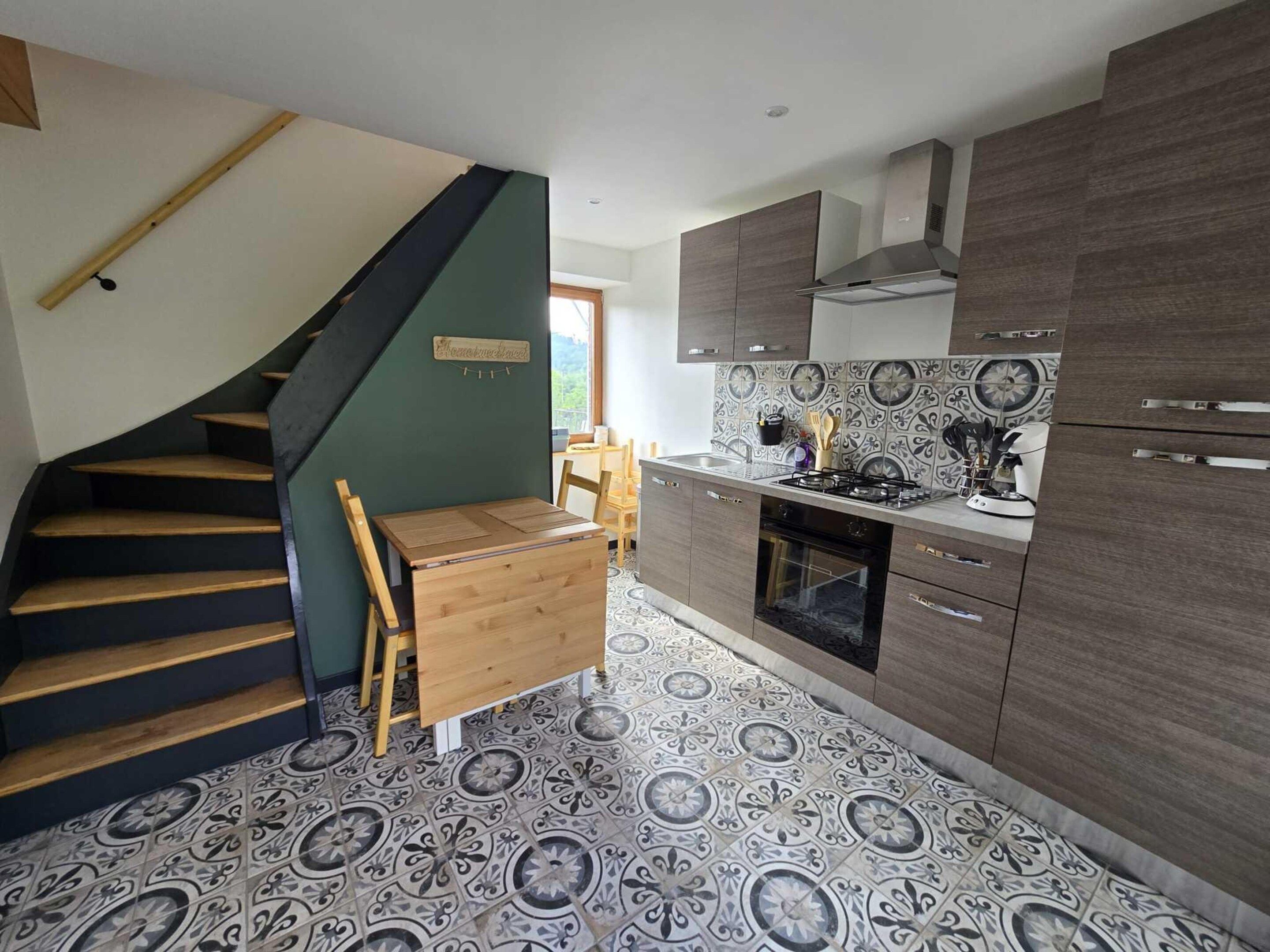 Una cocina con una escalera de madera, una mesa de comedor y baldosas de suelo con diseño.